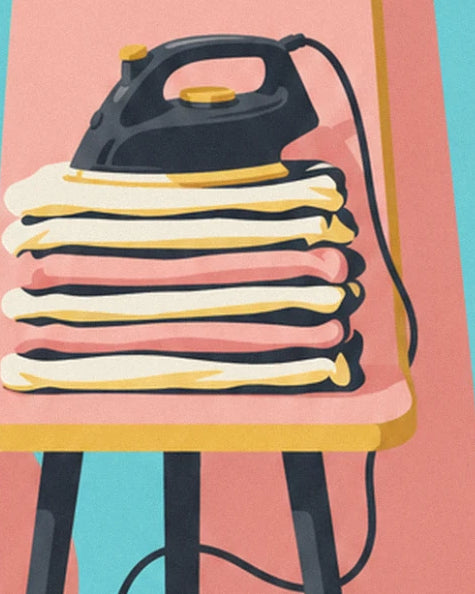 The black iron resting on a pile of cream, pink and yellow laundry on the ironing board