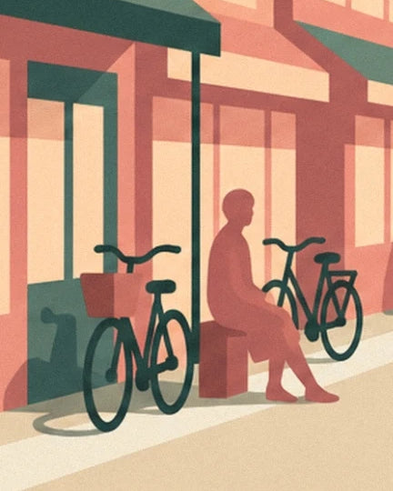 A seated figure between 2 bicycles, in front of coral-coloured shop windows