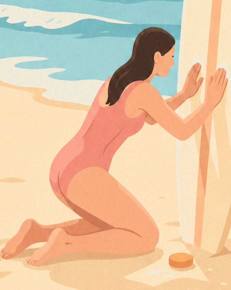 La surfeuse en maillot corail, à genoux devant sa planche, et son pain de cire sur le sable